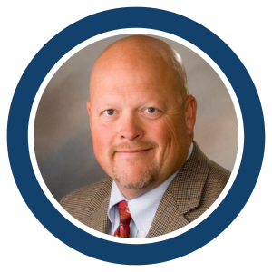 A bald man with light skin, wearing a brown checked suit jacket, light blue shirt, and red tie, is smiling slightly. The photo is framed by a blue and white circular border, representing Joe Buy Houses and their reliable cash offer service.